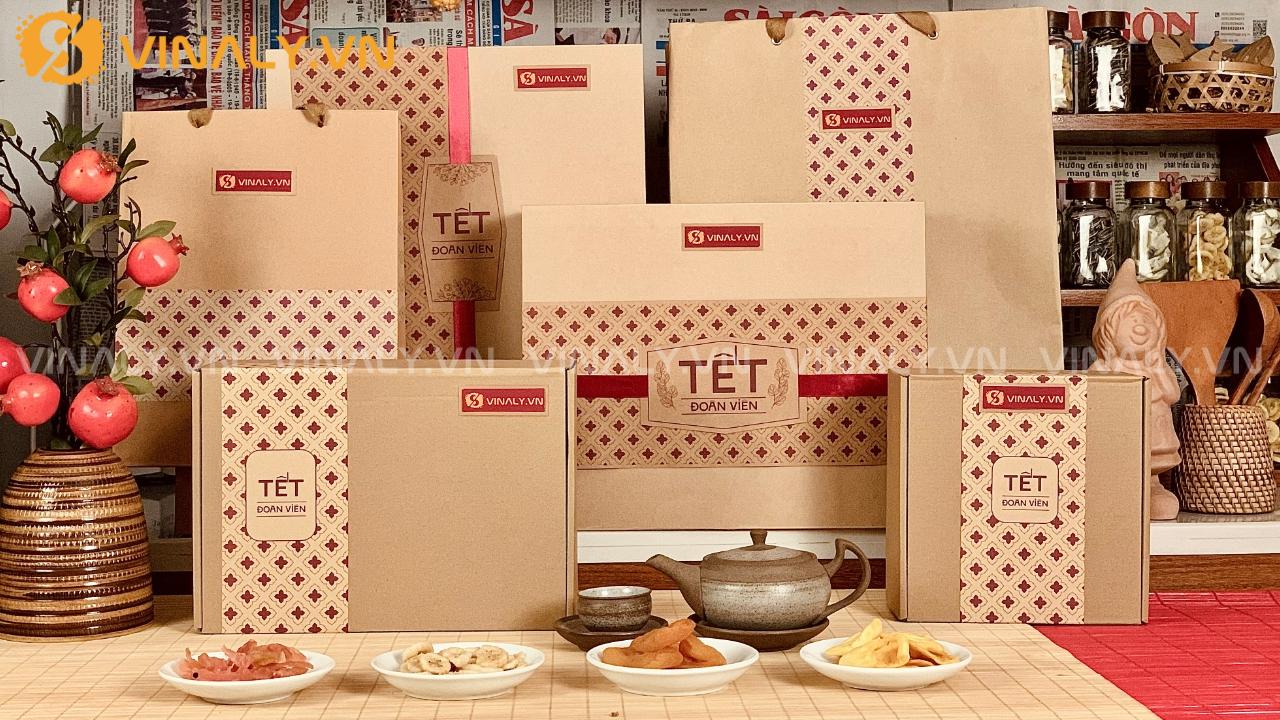 Bộ sưu tập giỏ quà Tết Đoàn Viên 2026 của Vinaly với thiết kế hộp kraft cao cấp, tông màu nâu đỏ truyền thống, trưng bày trên bàn gỗ cùng trái cây và ấm trà. Bao gồm nhiều kích thước hộp quà Tết phù hợp cho doanh nghiệp và cá nhân.