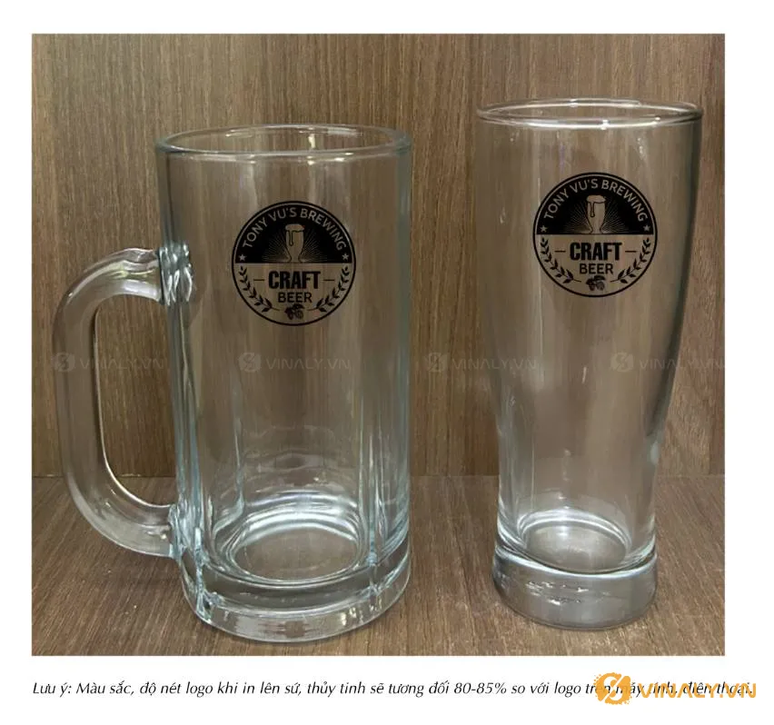 Hai ly bia thủy tinh trong suốt, một có quai và một dáng cao, in logo "TONY VU'S BREWING" đen. Ly bia thủy tinh in logo