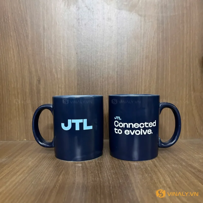 Hai ly sứ trụ xanh cửu long in logo JTL trắng nổi bật, đặt trên nền gỗ, thể hiện sự chuyên nghiệp và tinh tế của quà tặn