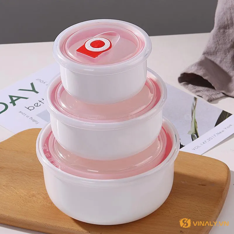 Bộ thố sứ hút chân không gồm ba chiếc (S,M,L) xếp chồng lên nhau 1 Bộ thố sứ hút chân không in logo gồm ba chiếc màu trắng, nắp hồng trong suốt, xếp chồng lên nhau trên thớt gỗ, sẵn sàng làm