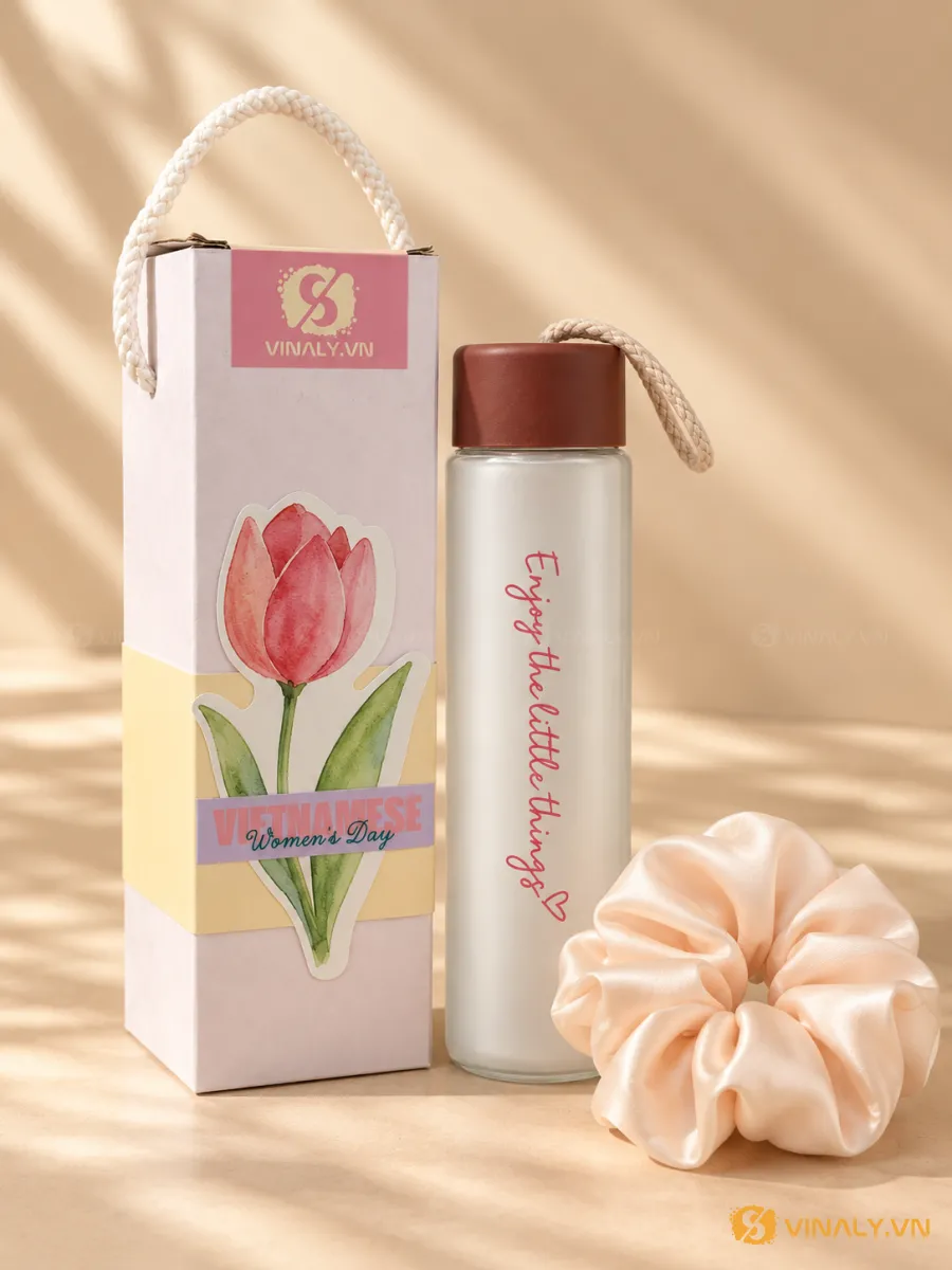 Bình nước thủy tinh nắp nâu in logo chữ 'Enjoy the little things' màu hồng, kèm scrunchie hồng nhạt và hộp quà trang trí hoa