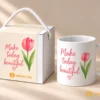 Set Quà Tặng Nhân Viên Nữ 20/10 Hay chỉ 99k 1 Ly sứ trắng quai C in logo hình hoa tulip hồng và chữ, đặt cạnh hộp quà trắng có quai xách dây thừng, tạo bộ quà tặng tinh