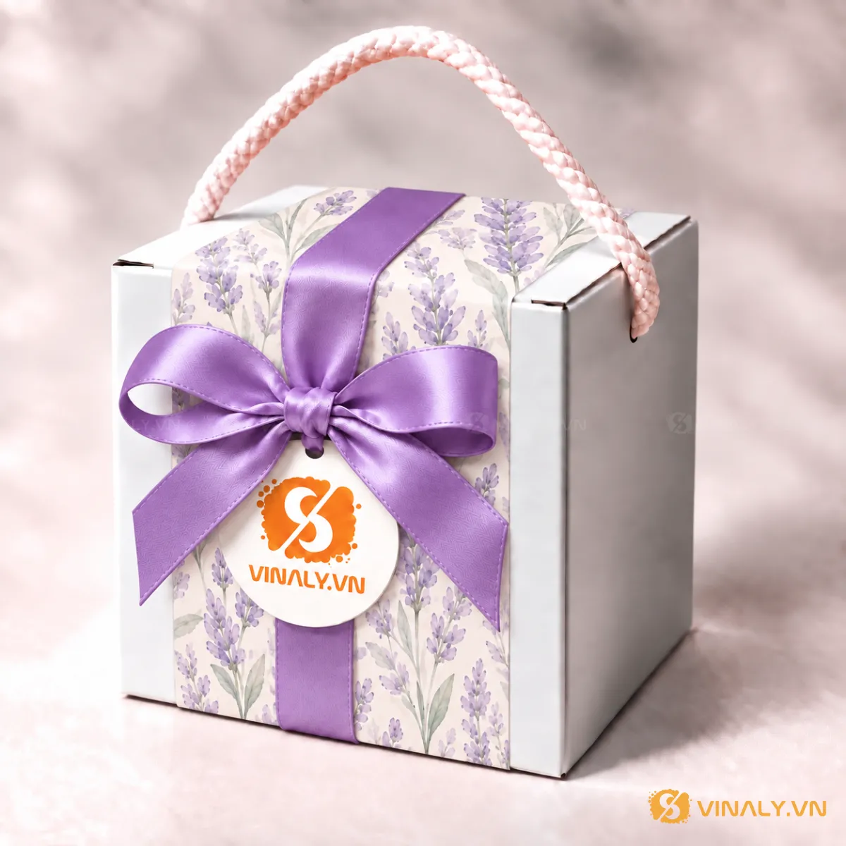 Set Quà Tặng Ly Sứ Cao Cấp Phụ Nữ 20/10 8/3 22 Hộp quà tặng in logo Vinaly màu trắng với họa tiết hoa lavender tím, nơ lụa màu tím và quai xách hồng, có tag thương hiệu.