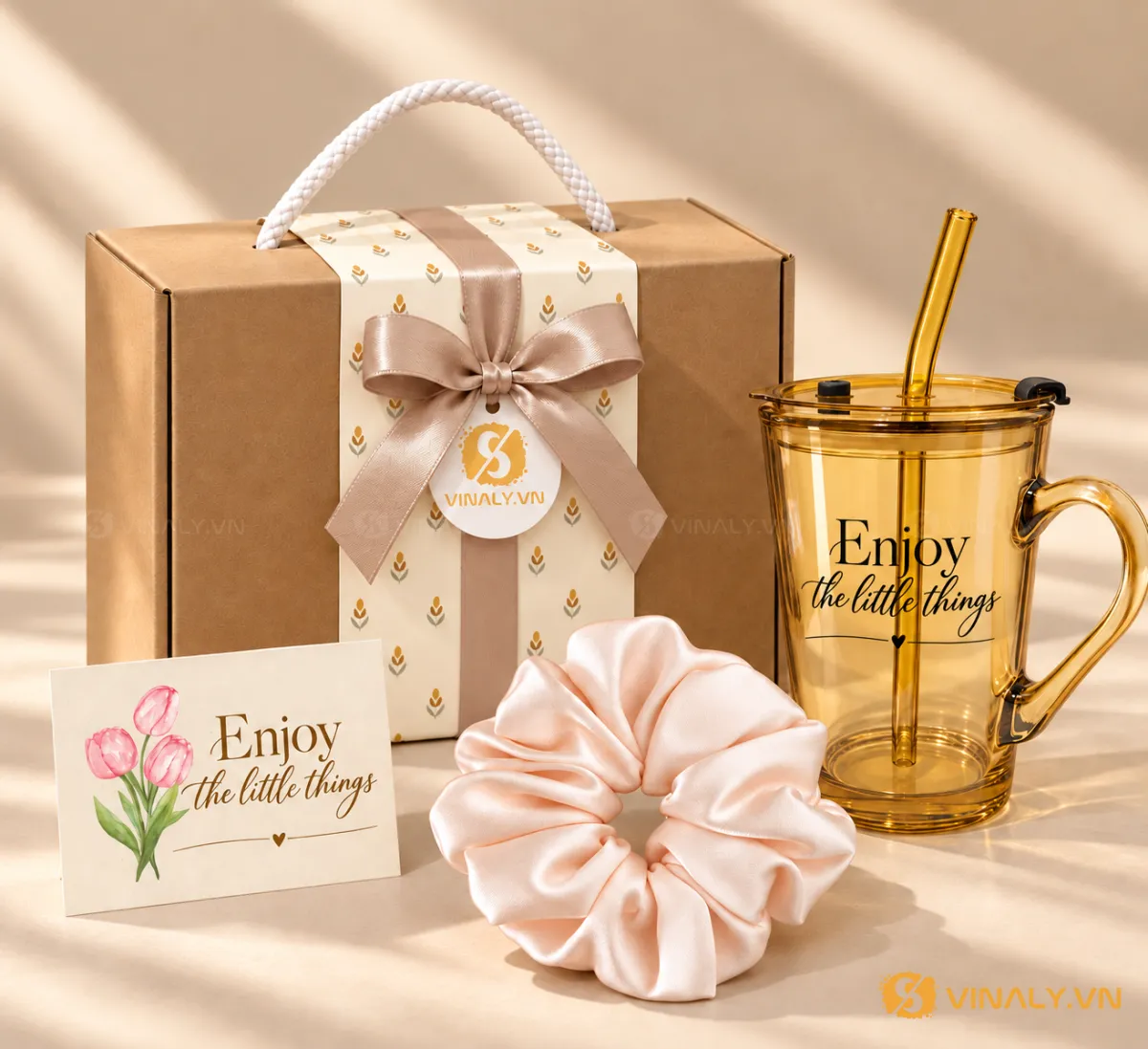 Ly nhựa có quai ống hút in logo màu hổ phách, có ống hút, in chữ "Enjoy the little things", kèm scrunchie hồng và hộp quà