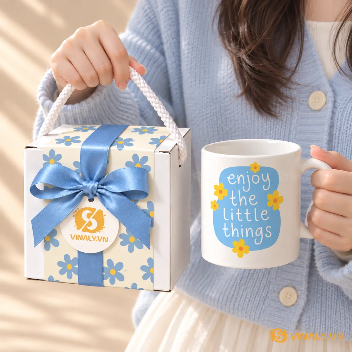 Set Quà Tặng Ly Sứ Cao Cấp Phụ Nữ 20/10 8/3 10 Cô gái cầm ly sứ trắng in hình in logo với họa tiết hoa xanh vàng và hộp quà đồng bộ, món quà ý nghĩa cho doanh nghiệp.